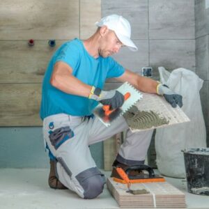 Worker in blue shirt applying adhesive for tile installation in a modern bathroom.