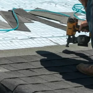 What does a roofing contractor do? Here a roofing contractor uses a pneumatic nailer to attach shingles to a roof