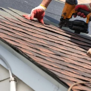 roofer installing asphalt shingles with a pneumatic nailer