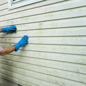 Hands wearing blue gloves cleaning dirty vinyl siding