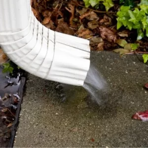 A close-up image of a white downspout attached to a home, with water flowing from it.