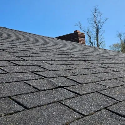 asphalt roof shingles in sunlight with a clear blue sky and a brick chimney in the background