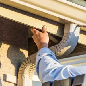 Contractor securing a rain gutter to a house, ensuring proper installation and alignment.