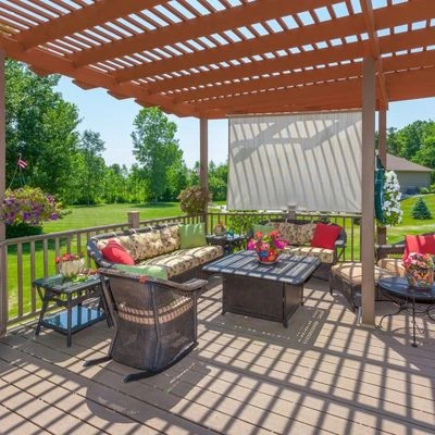 pergola-deck-partial-shade-seating-area Wooden pergola structure over deck creating dappled shade for outdoor seating area with wicker furniture and fire table