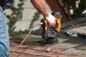 pneumatic-nailer-shingle-installation Roofer using a nail gun to install asphalt shingles on a roof.