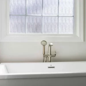 Modern bathtub faucet with handheld sprayer positioned beneath a white-framed window